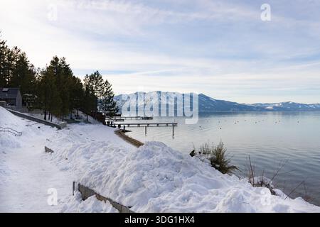 Un sentier couvert de neige mène au lac de South Lake Tahoe. Les bateaux sont amarrés à un quai tandis que des montagnes enneigées s'élèvent en arrière-plan. La scène Banque D'Images