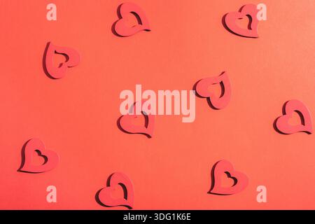 Formes de coeur en bois dispersées sur fond rouge. Concept de la Saint-Valentin, modèle. Banque D'Images
