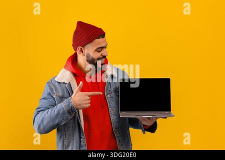 L'homme tient l'ordinateur portable et les points tout en se tenant devant le fond jaune Banque D'Images