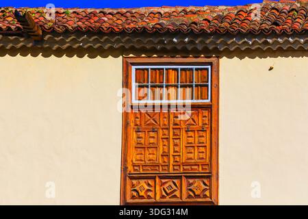 Façade de bâtiment traditionnelle avec porte en bois sculpté sertie dans un mur en stuc, surmontée de tuiles de toit en argile rouge. Le ciel bleu améliore les tons terreux et la cr complexe Banque D'Images
