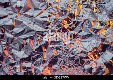 Texture de feuille d'aluminium froissée avec reflets de lumière orange chaud Banque D'Images