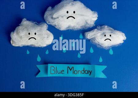 Composition Creative Blue Monday mettant en vedette des nuages de coton avec des visages tristes, des gouttes de pluie en papier et une bannière sur un fond bleu. Banque D'Images