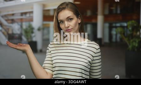 Femme tient la main ouverte paume tournée vers le haut dans le bâtiment moderne spacieux ; question d'incertitude d'enquête de curiosité. Banque D'Images