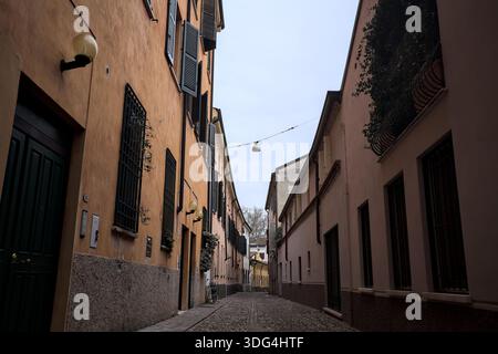 Étroite ruelle pavée avec des façades de bâtiments bas à l'ombre sur une journée nuageuse dans une ville italienne Banque D'Images