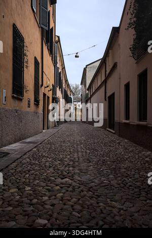 Étroite ruelle pavée avec des façades de bâtiments bas à l'ombre sur une journée nuageuse dans une ville italienne Banque D'Images