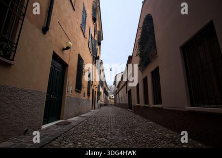 Étroite ruelle pavée avec des façades de bâtiments bas à l'ombre sur une journée nuageuse dans une ville italienne Banque D'Images