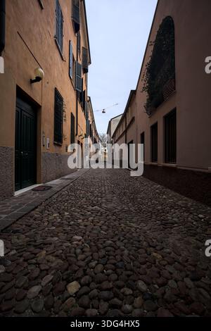 Étroite ruelle pavée avec des façades de bâtiments bas à l'ombre sur une journée nuageuse dans une ville italienne Banque D'Images