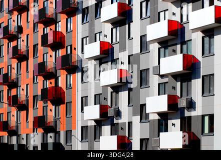 Façade d'un bâtiment résidentiel moderne avec blocs de couleurs audacieux, panneaux de balcon rouges et blancs, sections murales gris foncé et orange, géome minimaliste Banque D'Images