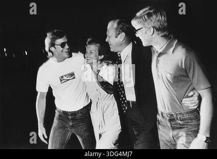 Cette photographie vintage en noir et blanc des années 1970 capture l'ancien président Gerald Ford et la première dame Betty Ford en profitant d'un moment de légèreté avec leurs fils Jack et Steven. La famille est montrée souriante et embrassante, suggérant une occasion décontractée et joyeuse. Banque D'Images