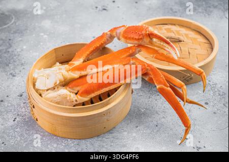 Cuisses de crabe rouge kamchatka de luxe servies dans un cuiseur vapeur en bambou sur fond texturé léger composition de fruits de mer gastronomique. Banque D'Images