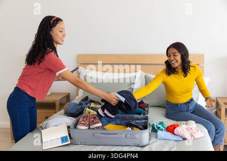 Maman diversifiée et fille adolescente organisant des vêtements dans la chambre avec valise ouverte et baskets Banque D'Images