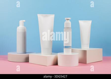 Beaux modèles cosmétiques pour les annonces, tubes de crème en plastique et bouteilles sur un fond bleu avec des podiums. Design esthétique pour un produit haut de gamme Banque D'Images