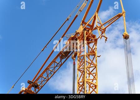 Grue de construction jaune avec des câbles métalliques fixés contre un ciel bleu vif Banque D'Images