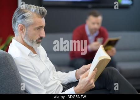 La clientèle masculine avec téléphone en attente à salon de coiffure Banque D'Images
