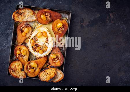 camembert cuit au four avec poires glacées caramélisées, noix et raisins et baguette servie sur une assiette en métal rustique Banque D'Images