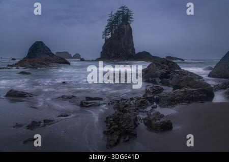Vue sur Ruby Beach, parc national olympique, avec de grandes couches de roche et de l'eau de mer brumeuse sous un ciel sombre et nuageux au crépuscule. Banque D'Images