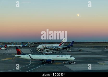 New York City, NY, États-Unis-4 novembre 2025 ; avion Delta remorqué par tracteur d'avion jusqu'à la porte d'embarquement de l'aéroport JFK au crépuscule avec ciel orange et pleine lune Banque D'Images