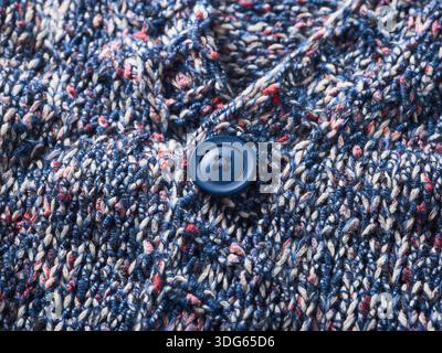 Gros plan d'un bouton bleu sur un tricot texturé multicolore. Banque D'Images