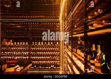 Une cave à vin faiblement éclairée avec des étagères pleines de bouteilles de vin sous un éclairage ambiant chaud. Guangzhou, Guangdong, Chine Banque D'Images