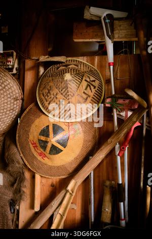 Chapeaux tissés traditionnels et outils de jardinage disposés sur un fond de mur en bois. Voyage de Guilin à Chengdu, Guangxi, Sichuan, Chine Banque D'Images