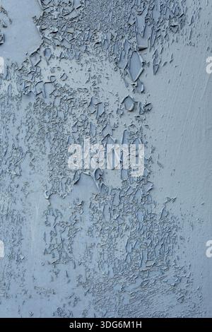 Vieille surface peinte avec peinture pelable et texture inégale. Les couleurs vont du bleu clair au gris, avec un matériau de base exposé dans certaines zones. Banque D'Images