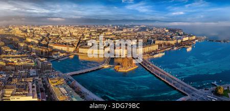Vue aérienne panoramique de l'horizon de la ville et du lac de Genève, en Suisse, lors d'un lever de soleil d'hiver doré avec brouillard et nuages Banque D'Images