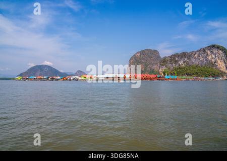 Koh Panyee. Février 2025, Thaïlande. Village de pêcheurs côtier avec fermes piscicoles flottantes et maisons colorées sous d'imposantes falaises de calcaire Banque D'Images