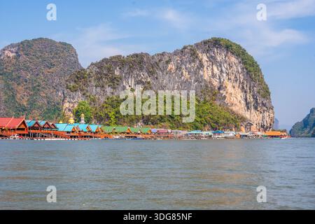 Koh Panyee. Février 2025, Thaïlande. Village de pêcheurs côtier avec fermes piscicoles flottantes et maisons colorées sous d'imposantes falaises de calcaire Banque D'Images
