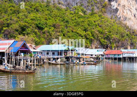 Koh Panyee. Février 2025, Thaïlande. Village de pêcheurs côtier avec fermes piscicoles flottantes et maisons colorées sous d'imposantes falaises de calcaire Banque D'Images
