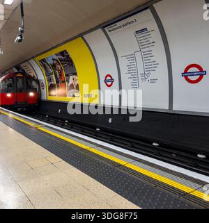Train de métro londonien arrivant à la station Knightsbridge sur la ligne Piccadilly avec signalisation du tunnel et publicité visible sur le mur du quai Banque D'Images