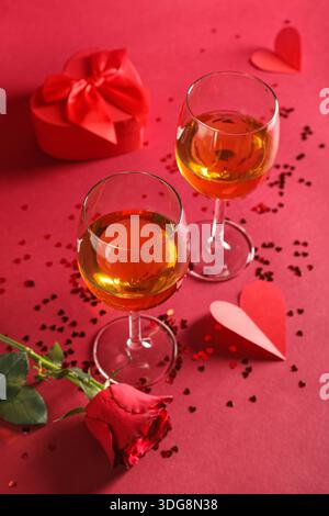 Verres de vin avec boîte-cadeau, coeurs en papier et fleur de rose sur fond rouge. Célébration de la Saint-Valentin Banque D'Images