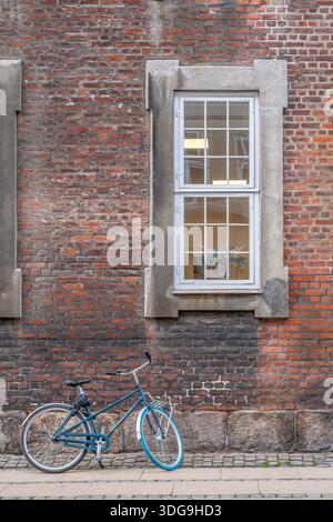 Blue City Bicycle garé contre un vieux mur de briques rouges avec fenêtre blanche, Urban Lifestyle, Copenhague, Danemark Banque D'Images