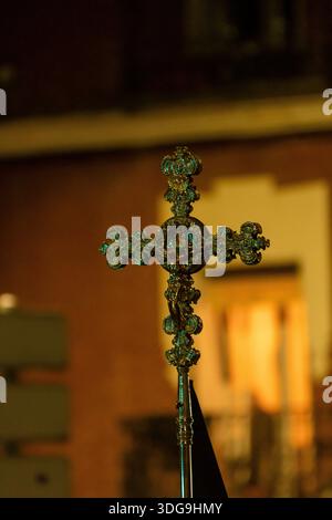 Une croix magnifiquement travaillée se détache sous un éclairage tamisé lors d'une procession religieuse nocturne dans une ville. Banque D'Images