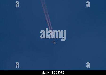 Avion volant haut créant des traînées à travers le ciel bleu profond Banque D'Images