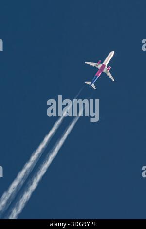 Avion à réaction de passagers naviguant en altitude, créant deux traînées blanches contre un ciel bleu profond Banque D'Images