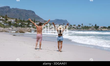 Un couple se promène le long des rives sablonneuses de camps Bay, Cape Town, profitant du soleil et des vagues. Les montagnes offrent une superbe toile de fond, parfaite pour un Banque D'Images