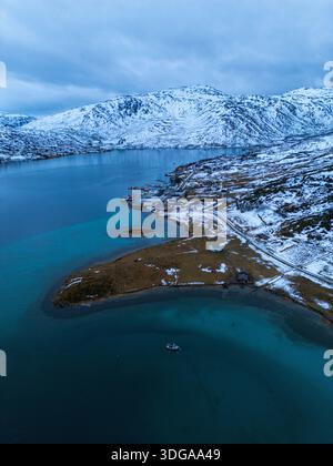 Vue aérienne du fjord serein embrassant les montagnes enneigées, un paysage tranquille où les eaux glacées rencontrent le terrain accidenté, Kvaløya, Troms Banque D'Images