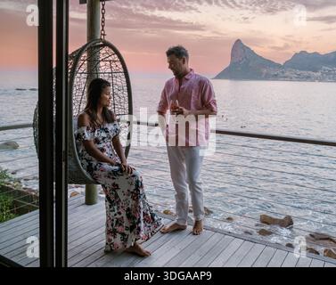 Un couple profite d’un moment de sérénité sur une terrasse en bois surplombant l’océan au coucher du soleil au Cap, en Afrique du Sud. Les belles montagnes du Cap créent une photo Banque D'Images