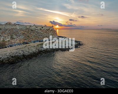Vue aérienne du coucher de soleil derrière la Fortezza de Réthymnon comme il jette une lueur dorée sur la mer sombre et ondulante, Rethimno, Réthymnon, Grèce. Banque D'Images