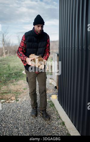 L'homme transporte du bois de chauffage près d'un bâtiment dans une zone rurale Banque D'Images