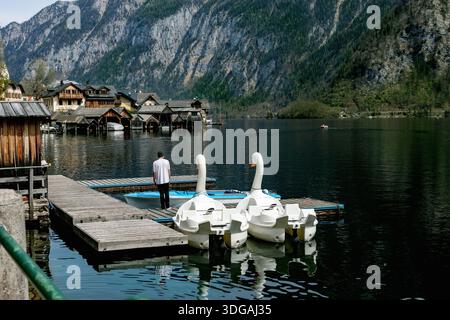Hallstatt Autriche. Quai en bois avec pédalos cygnes amarrés au lac de montagne. Personne debout sur la jetée du village au bord du lac avec boathou traditionnel en bois Banque D'Images