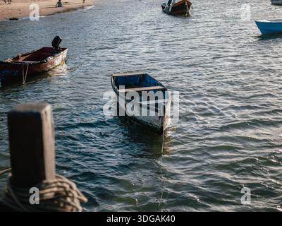 Petit bateau amarré dans l'eau côtière peu profonde près d'une plage par un jour couvert. Banque D'Images