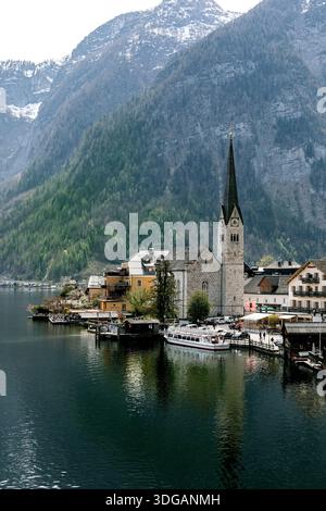 Vue pittoresque de l'église historique avec une grande flèche dans le village de Hallstatt situé au bord d'un lac entouré de majestueuses montagnes alpines célèbres terres autrichiennes Banque D'Images