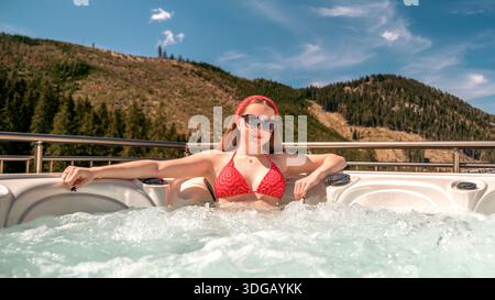 Jeune femme se relaxant dans un bain à remous extérieur avec vue sur la montagne profitant du bien-être et de la détente estivale Banque D'Images