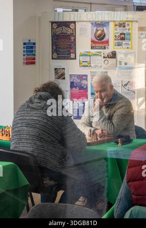 Deux personnes âgées jouant aux échecs photographiées à travers la fenêtre d'un centre social et d'activités à Newport sur l'île de wight au Royaume-Uni Banque D'Images