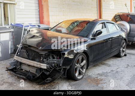 Voiture de luxe lourdement endommagée après un accident de la route, garée à l'extérieur en attente de réparation, avec impact visible à l'avant et dommages à la carrosserie Banque D'Images