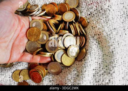 Gros plan de pièces en euros glissant entre les doigts d’une main. Monnaie dispersée sur la couverture de lit. Banque D'Images