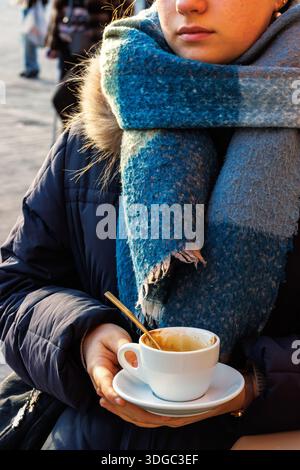 Jeune femme en manteau d'hiver tenant la tasse à café vide et la soucoupe à l'extérieur Banque D'Images