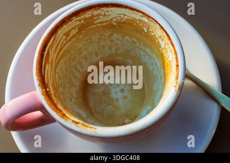 Videz la tasse à café avec les résidus de latte sur la soucoupe et versez à la cuillère à la lumière du soleil Banque D'Images