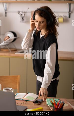 Jeune femme aux cheveux bouclés en vêtements décontractés s'engage avec son casque, absorbée dans ses pensées. Banque D'Images
